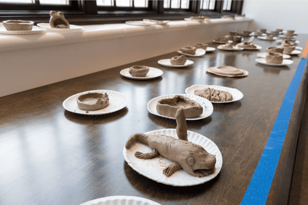 A collection of clay sculptures on paper plates arrayed on a table.