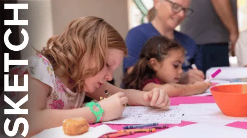 Children sitting at a table, focusing on sketching and coloring activities in a bright, indoor setting.