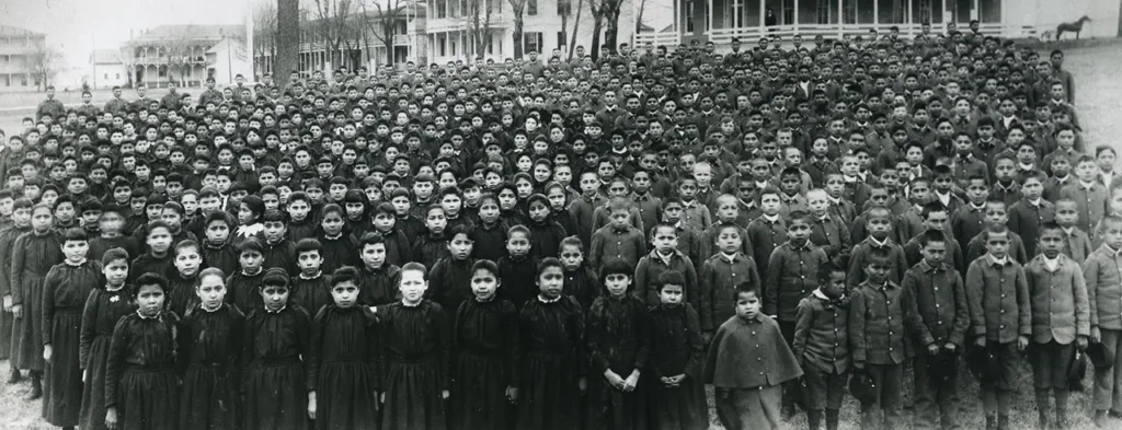 Black and white photo of school children in uniforms, black dresses on the girls and military style jackets and pants on the boys