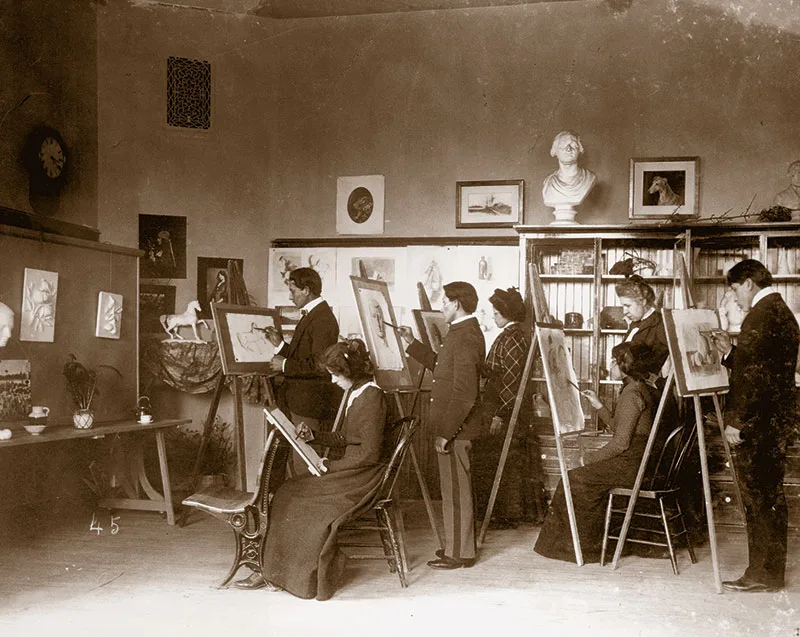 1900 black and white photo of young Native men and women at easels in a drawing still life objects