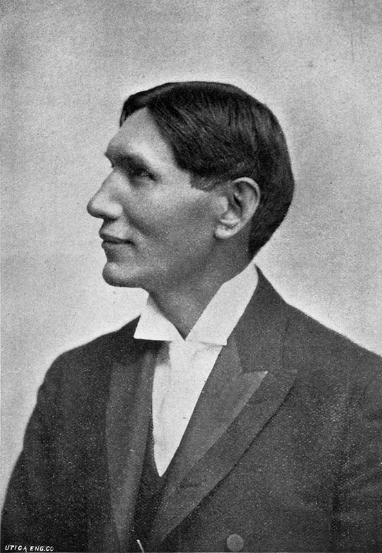 Black and white photo of a person in a suit and white tie, with short, neatly combed hair, looking to the left.