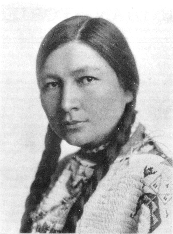 Black and white portrait of a woman with straight dark hair in two braids, wearing a patterned garment. She is looking directly at the camera with a neutral expression.