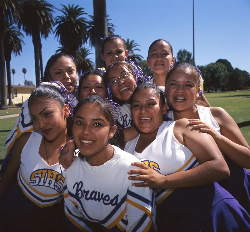 1999 candid color photo of young Native women in cheeleading outfits grouped tightly together and laughing and smiling for the camera