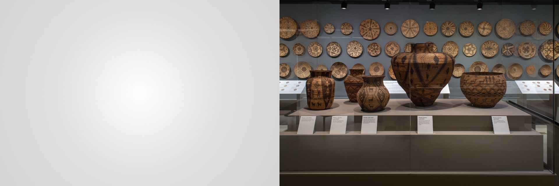 Display of intricately woven baskets and plates in a museum exhibit. The objects are arranged in a glass case with informational placards in front of them.