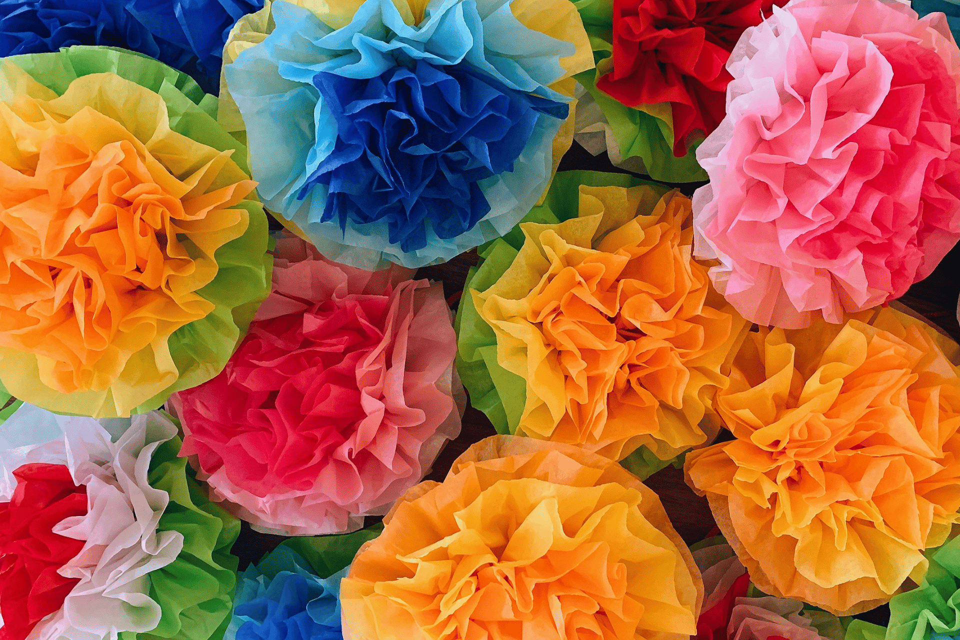 Close-up of vibrant, multicolored tissue paper flowers clustered together, featuring shades of yellow, red, pink, blue, green, and white.