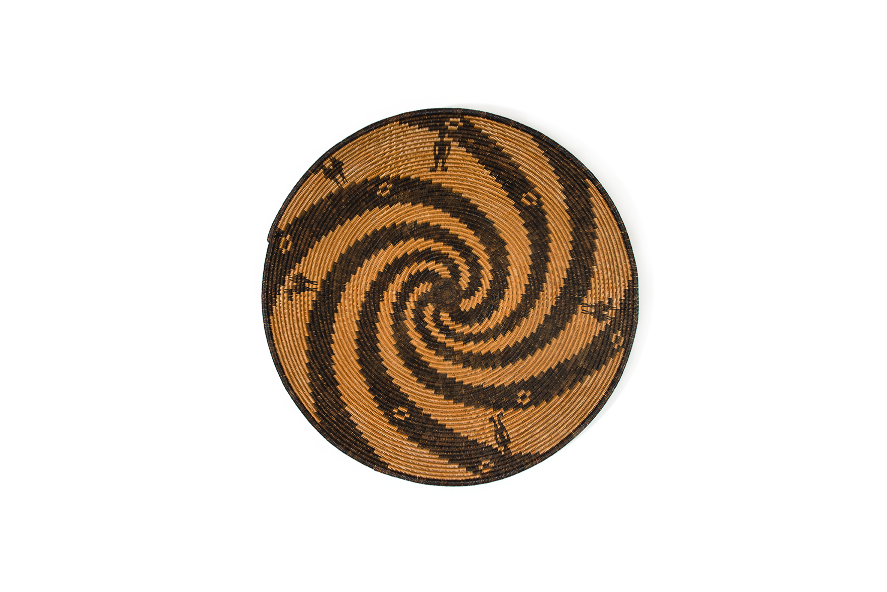 A round woven basket lid with a brown and black spiraling pattern and small black markings.