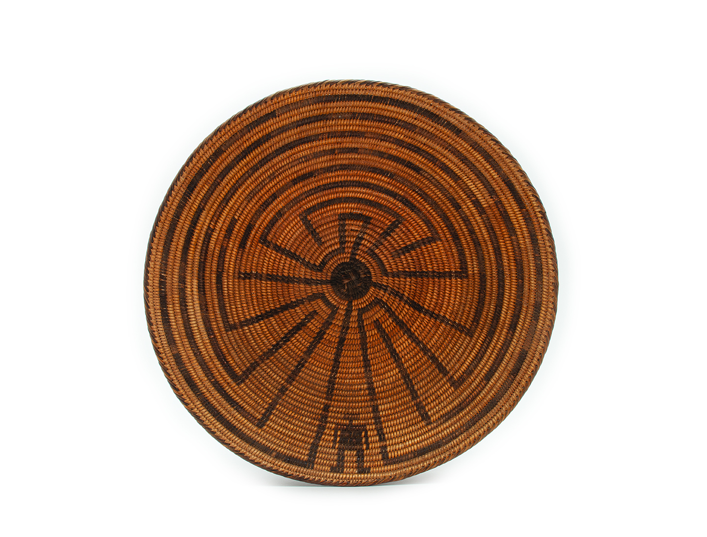 A round woven basket with a concentric pattern in shades of brown and black, displaying a symmetrical design in its center.