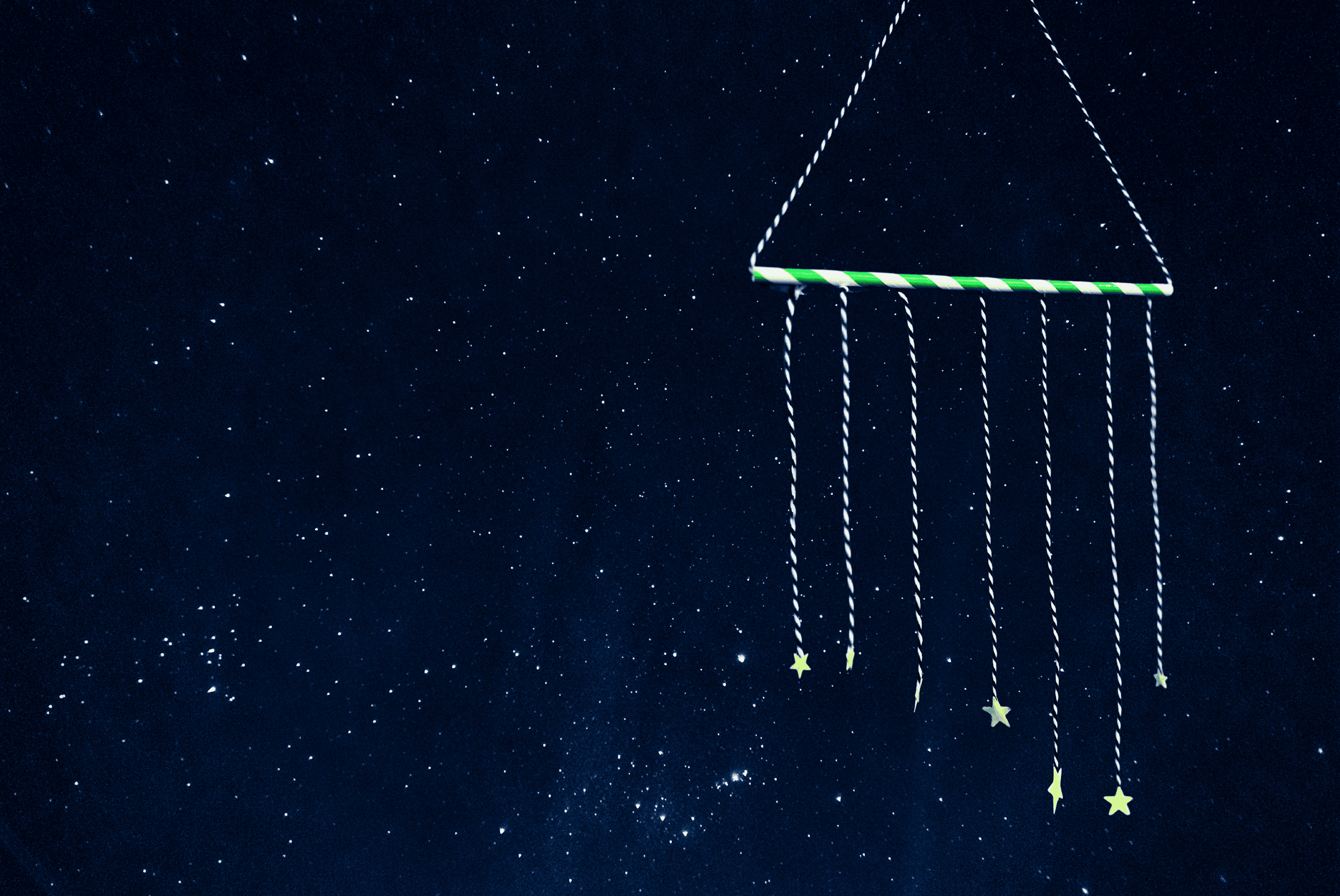 A triangular hanging mobile made of a green and white structure with strings and star shapes, set against a starry night sky.