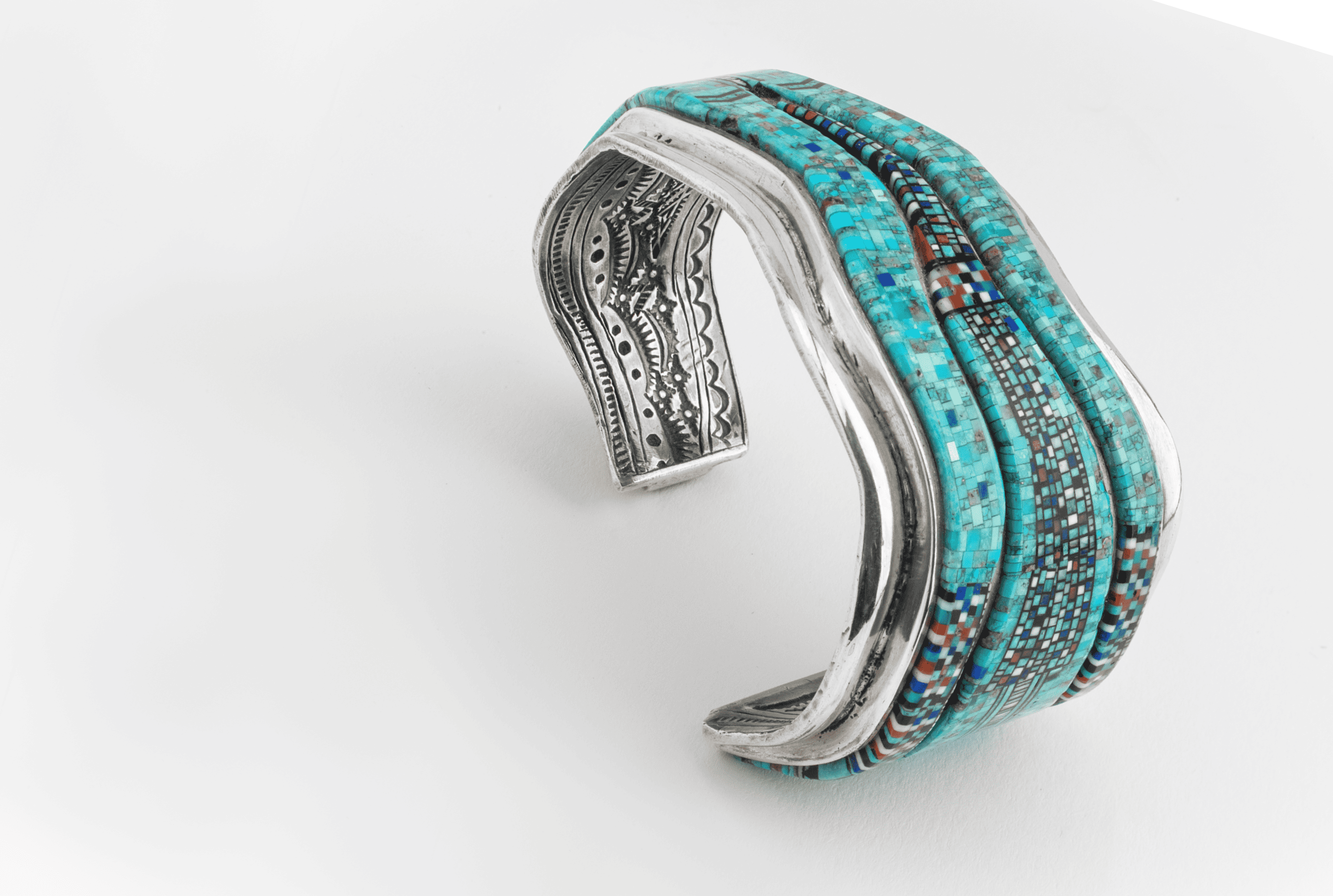 Silver cuff bracelet with turquoise and multicolored stone inlays, featuring intricate exterior engravings and a slightly curved, open-ended design.