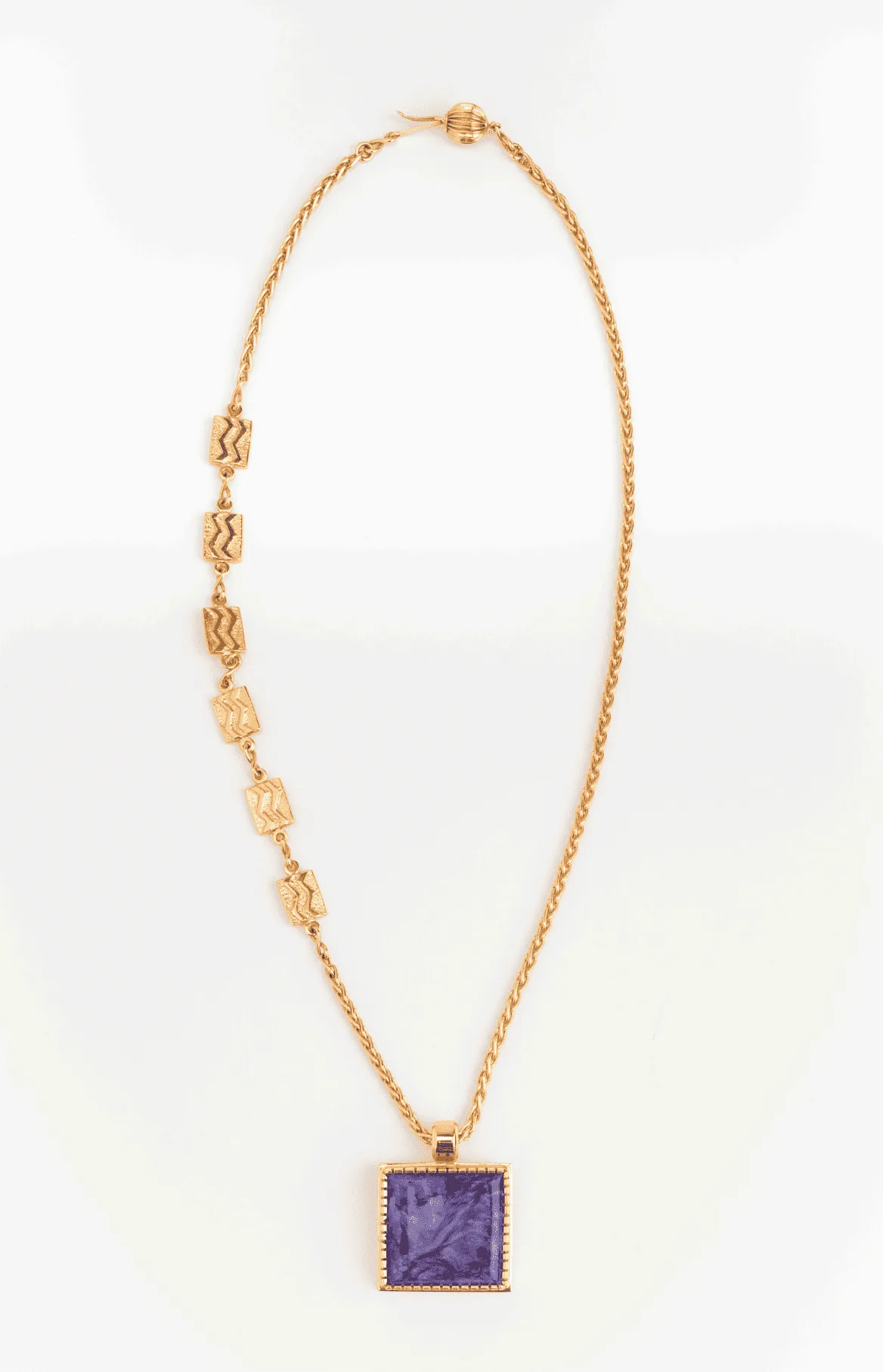 A gold chain necklace with geometric accents and a purple square pendant.