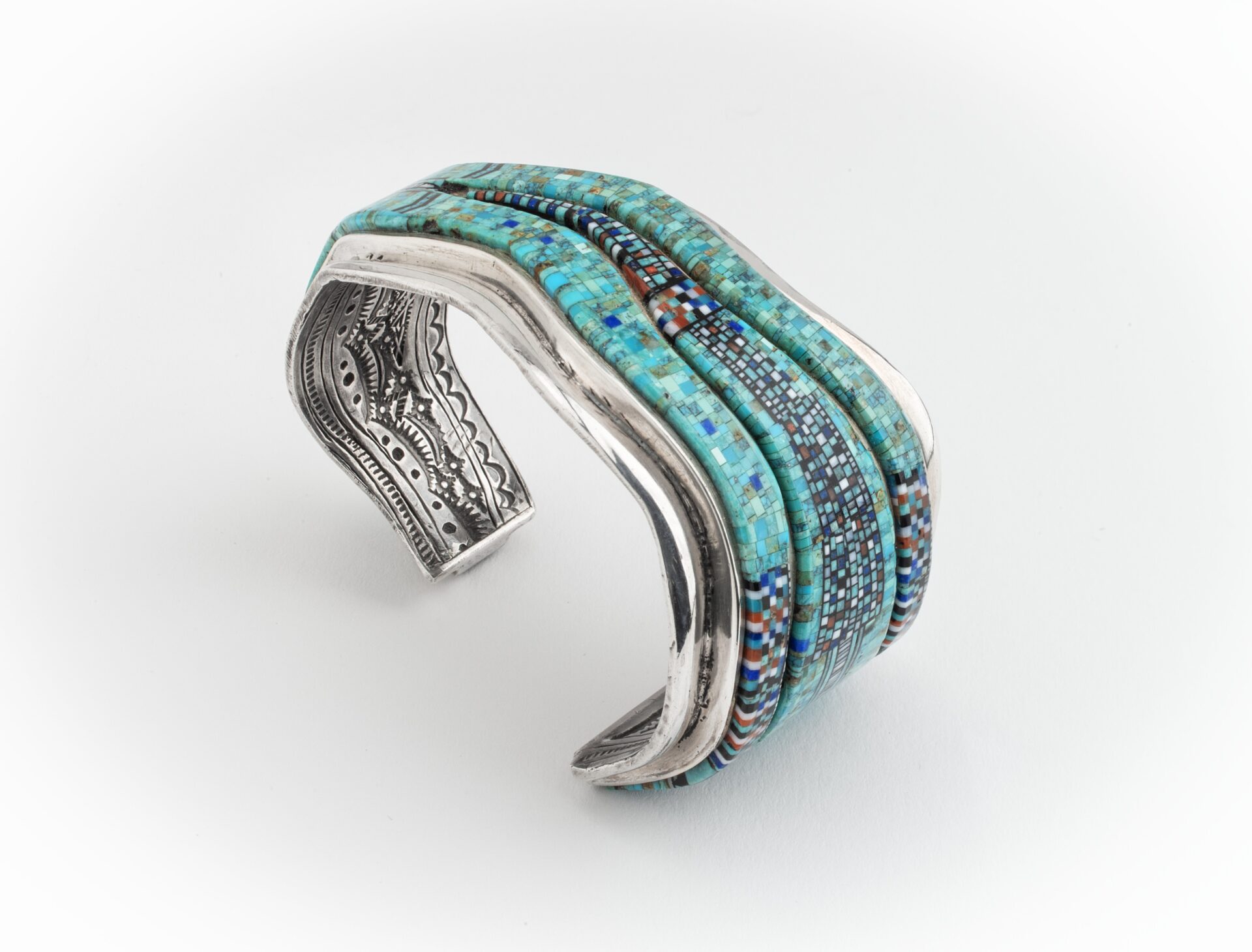 Silver cuff bracelet with intricate engravings and inlaid turquoise and multicolored beadwork, curved design.