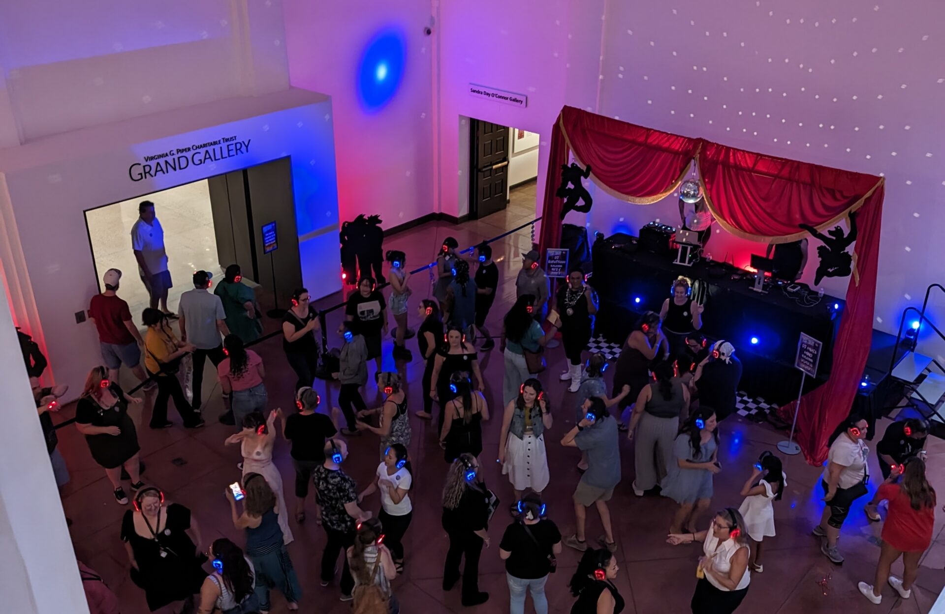 A group of people dancing and wearing headphones at a silent disco event in a room with red and blue lighting.