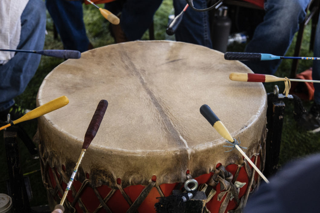 Close-up of a large drum surrounded by multiple drumsticks, showing hands poised to play.