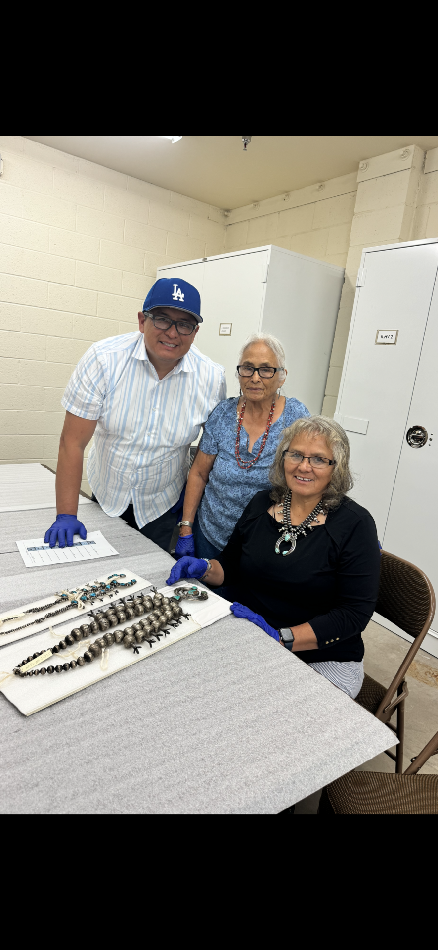 (L to R) Jay C. McCray with his grandmother Rose C. Begay and mother Marguerite McCray viewing works from the C.G. Wallace collection made by their family members Ch’ahii and Eva Chi Begay in the early 20th century. Jay is the 6th generation silversmith in his family. Photo courtesy of Jay C. McCray.