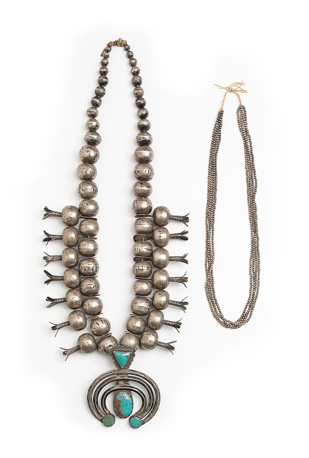 Left—Ch’ahii (Diné), Squash blossom necklace, 1923 (naja added in 1930). Silver, turquoise, 34 in. length. Gift of Mr. C. G. Wallace, Na-Sw-Na-J-295. Right—Eva Chi Begay (Diné), 4-strand necklace, collected in 1975. Silver, 24 in. length. Gift of Mr. C. G. Wallace, Na-Sw-Na-J-299. C.G. Wallace had commented on each of these necklaces that the beads were “the largest beads” and “the smallest beads” he had ever seen.