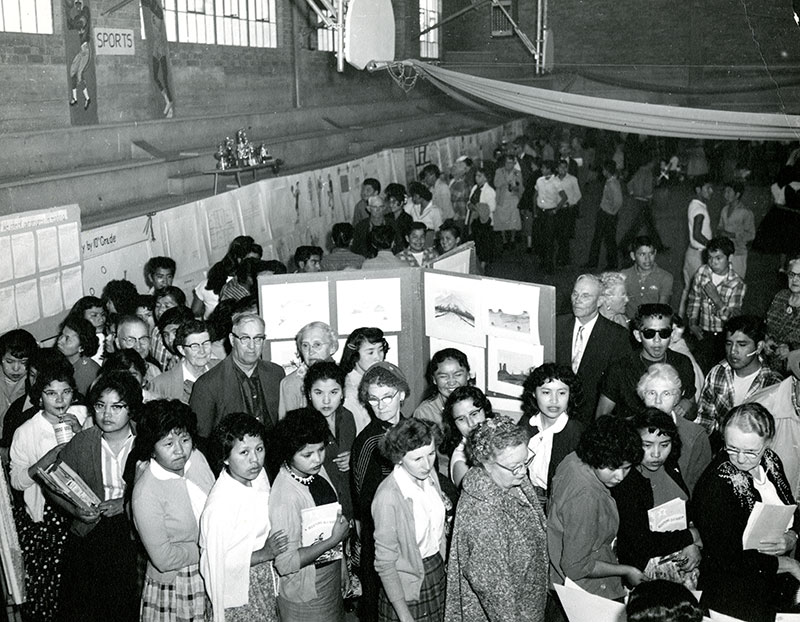 1950 black and white photo of a crowded room with art on panel boards and people looking at it