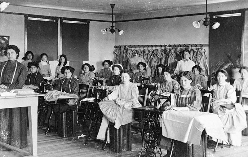 1900 black and white photograph of classroom with Native young women at sewing machines
